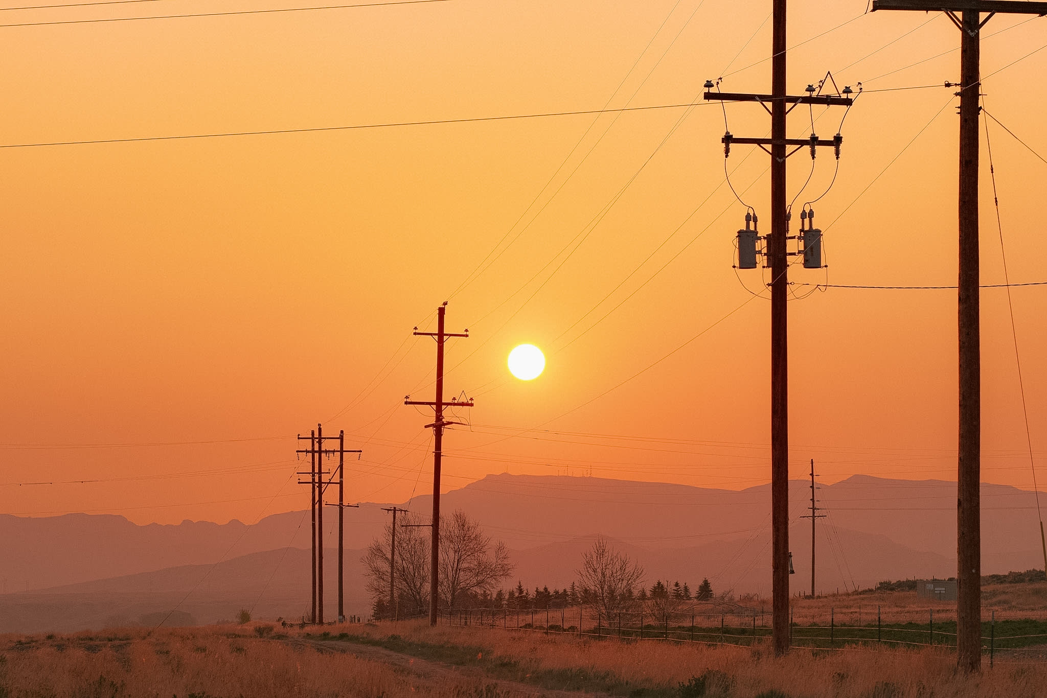 Power lines and poles against an orange sunrise
