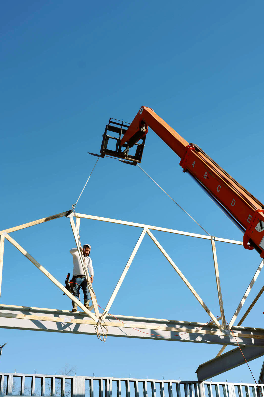 A worker guiding a roof truss as a crane lifts it into place